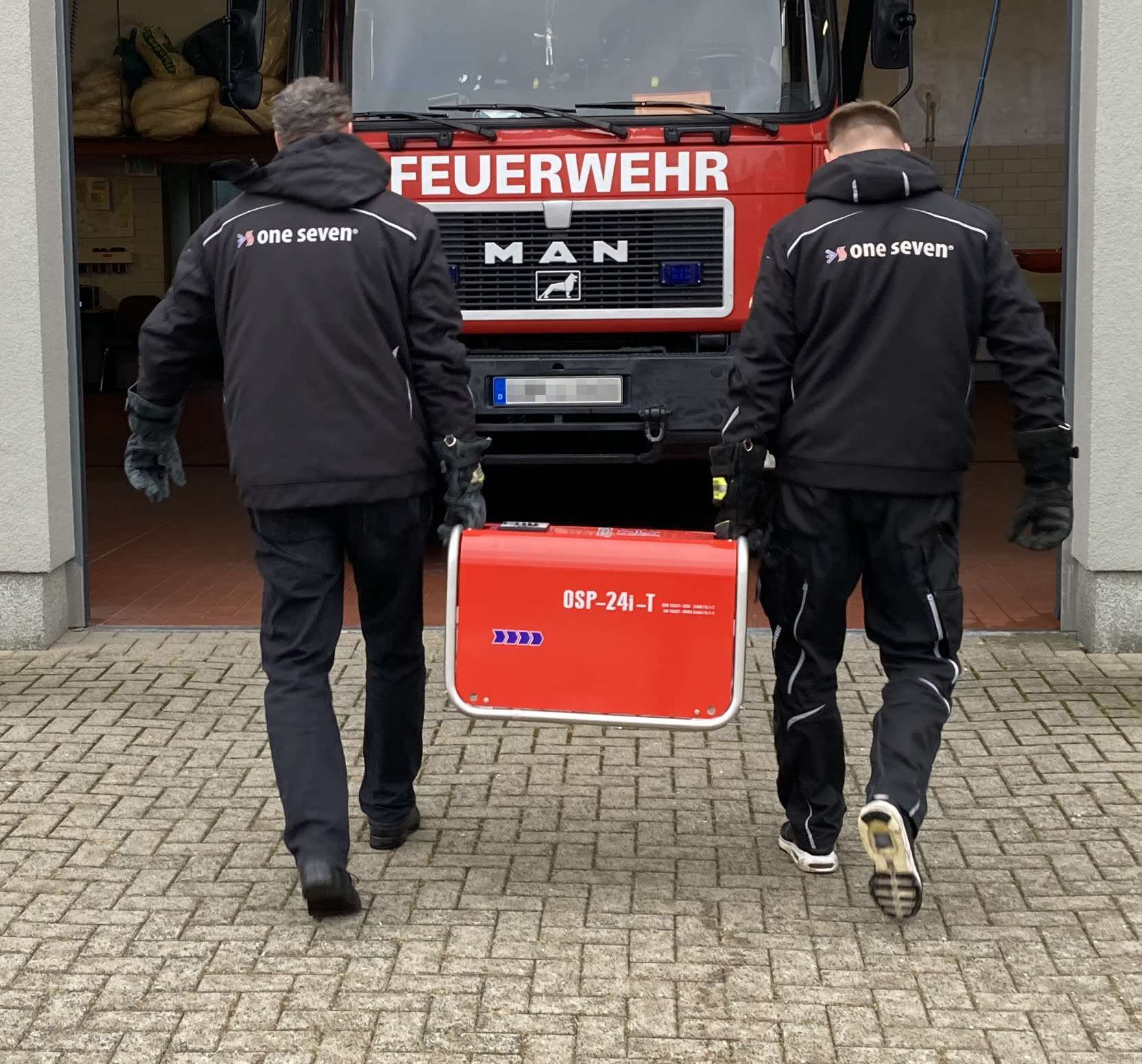Zwei Personen tragen den OSP-24i-T vor einem Feuerwehrfahrzeug
