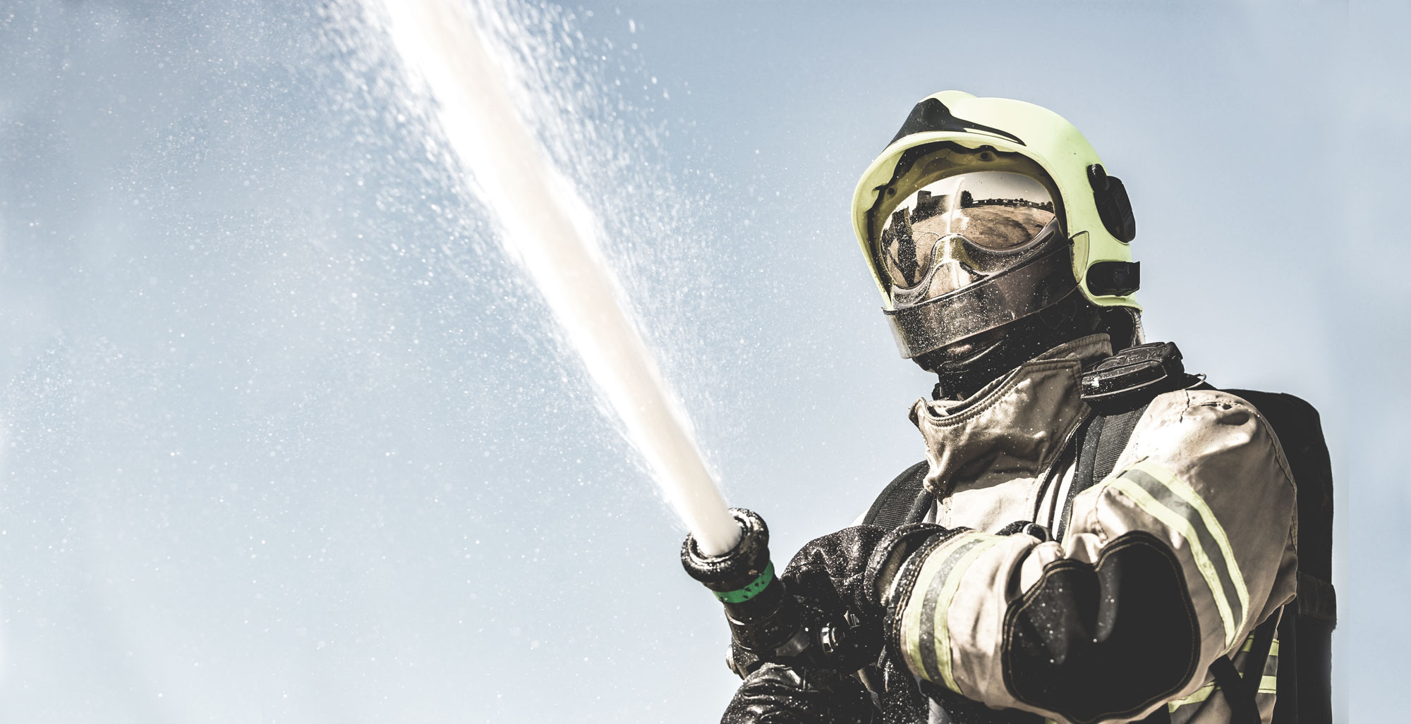 Feuerwehrmann in Atemschutzausrüstung mit Strahlrohr und Wasserstrahl