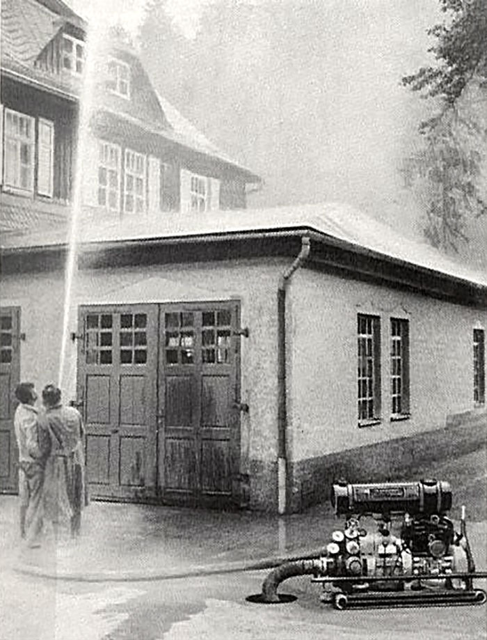 Historische Aufnahme eines Löscheinsatzes mit Wasserstrahl und Tragkraftspritze